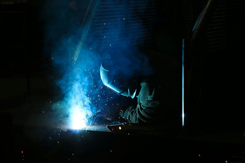a welder with helmet and equipment at work. Blue light, smoke and sparks around
