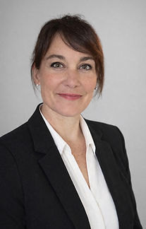 Woman with brown hair, wearing a black blazer, smiling.