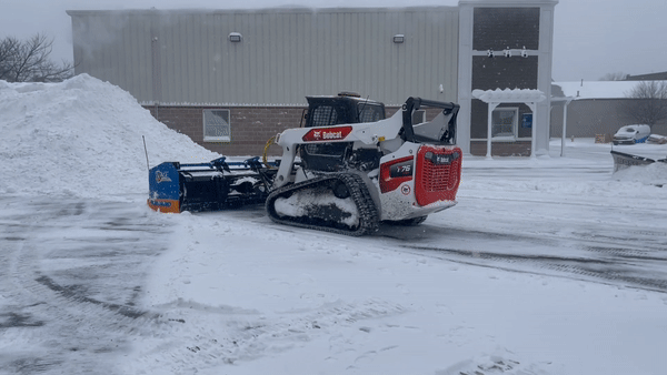 skid steer with plow attachment in action during a nor'easter storm 