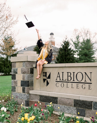 Portrait of Megan smiling in front of the Adrian College athletic field gates, a testament to her hard work and perseverance as a student-athlete.