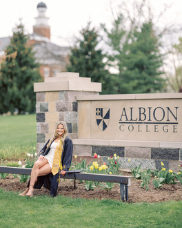 Scenic view of Megan posing in her graduation gown in front of the Adrian College athletic field gates, capturing the essence of her college journey.