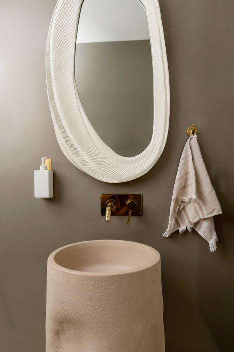 Modern minimalist bathroom with beige pedestal sink and abstract mirror design.