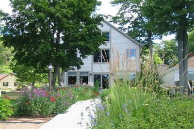 Contemporary white house among lush green trees and vibrant garden flowers.