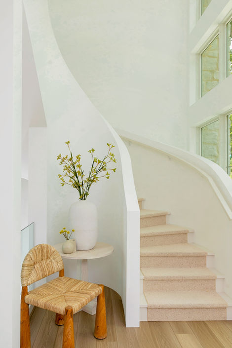 Modern spiral staircase, white walls, woven stool, and vase of flowers.