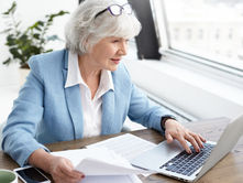 An experienced professional focuses intently while working on her laptop, surrounded by documents, in a bright, modern office space.