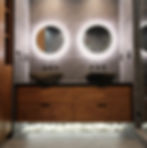 Modern bathroom with two round, backlit mirrors, vessel sinks, wooden cabinets, and white stones underneath in Barranca Dr. Monterey Park, CA.