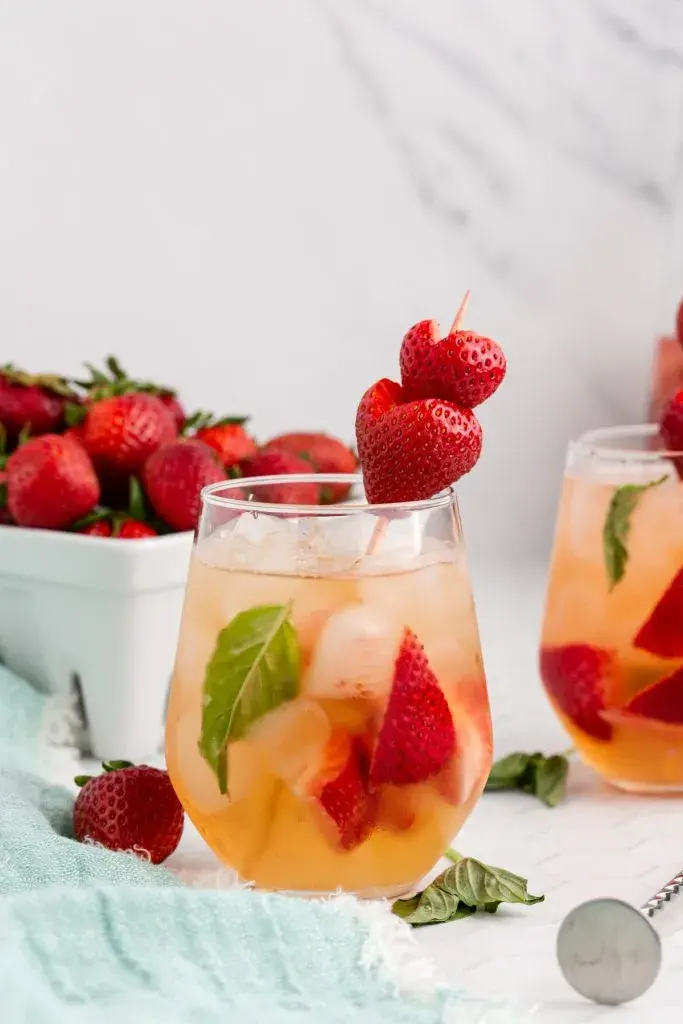 Fruity drink in a glass with ice, fresh strawberries, and mint, set on a light background with a basket of strawberries nearby. Refreshing vibe.