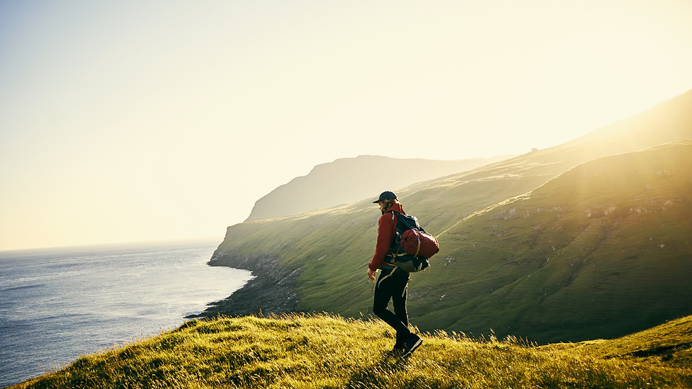 a man with a backpack is standing on a cliff overlooking the sea or ocean. The scene is sunny, and serene bringing a sense of calm and peace