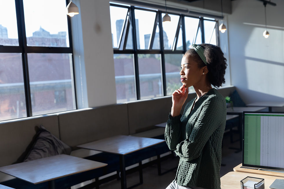 A professional pauses by a window at work, reflecting quietly amid ongoing responsibilities in an environment of constant change.