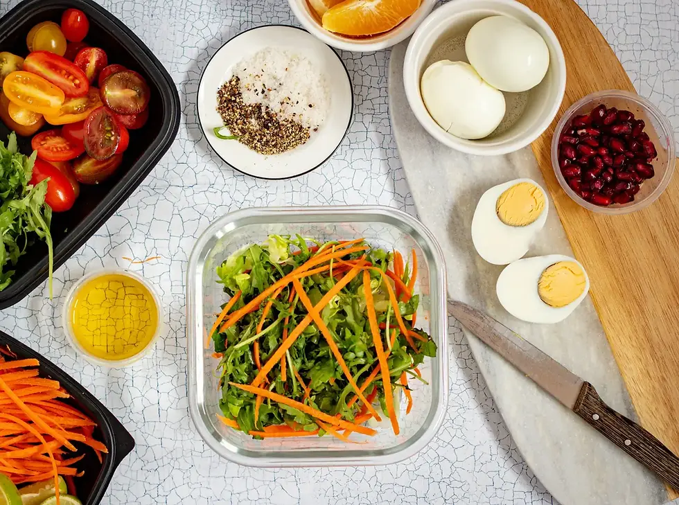 Glass meal prep containers with pasta, chicken, tomatoes, rice, eggs, and veggies, tailored for an anti-inflammatory Fibromyalgia Diet, arranged on a gray countertop with salt shakers and a green checkered cloth.