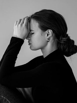 Thoughtful woman in black top with fibromyalgia rests her head on her hands, eyes closed, conveying emotional fatigue, pain management challenges, and the need for self-care in a calm, neutral environment.