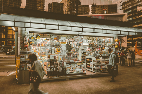 Beleuchteter Zeitungskiosk in einer urbanen Umgebung mit Passanten und moderner Architektur im Hintergrund