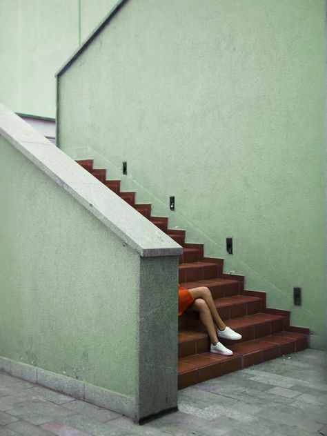 Kreative Aufnahme einer Person auf einer roten Treppe, modern inszeniert vor einer grünen Wand