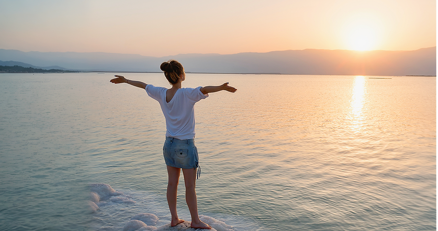 Woman standing on a beach at sunset with arms outstretched