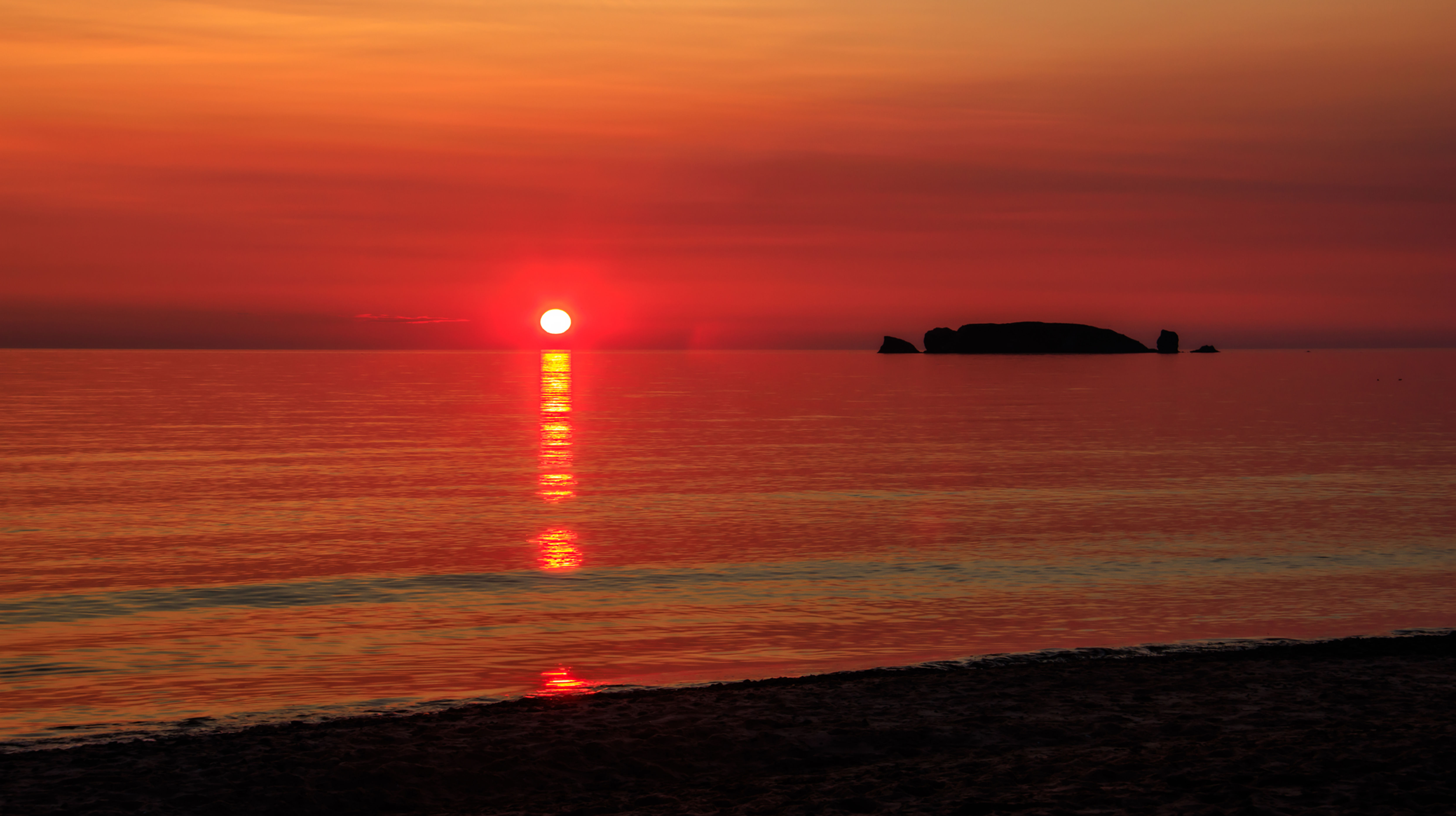 Magnifique coucher de soleil rouge sur l'océan, île rocheuse visible au loin.