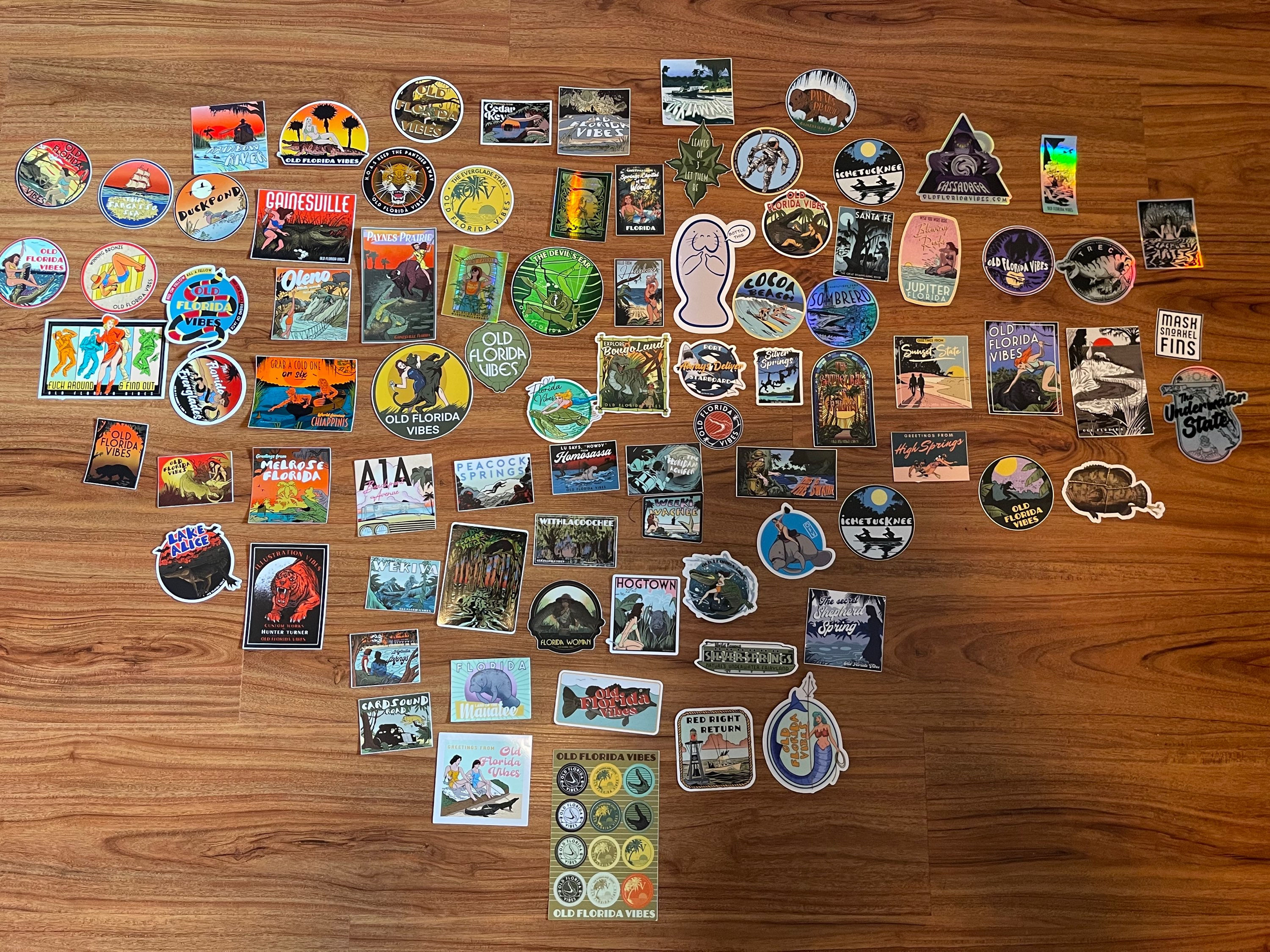 Collection of stickers on a wooden surface, various designs, outdoor theme stickers and logos.