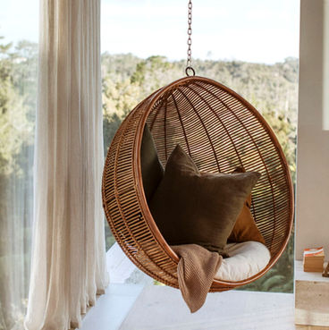 Cozy round hanging chair with pillows and blanket by a large window.