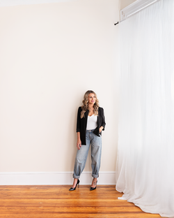 woman standing next to window, jeans and blazer