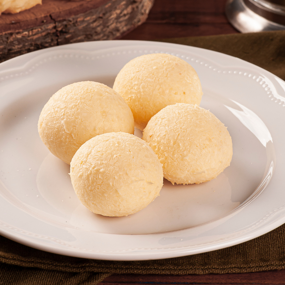 Four freshly baked Pan de Bono, a Colombian cheese bread filled with guava paste, on a white plate.