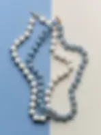 Three pastel beaded necklaces, white and blue, arranged on a split blue-and-cream background, neatly overlapping.