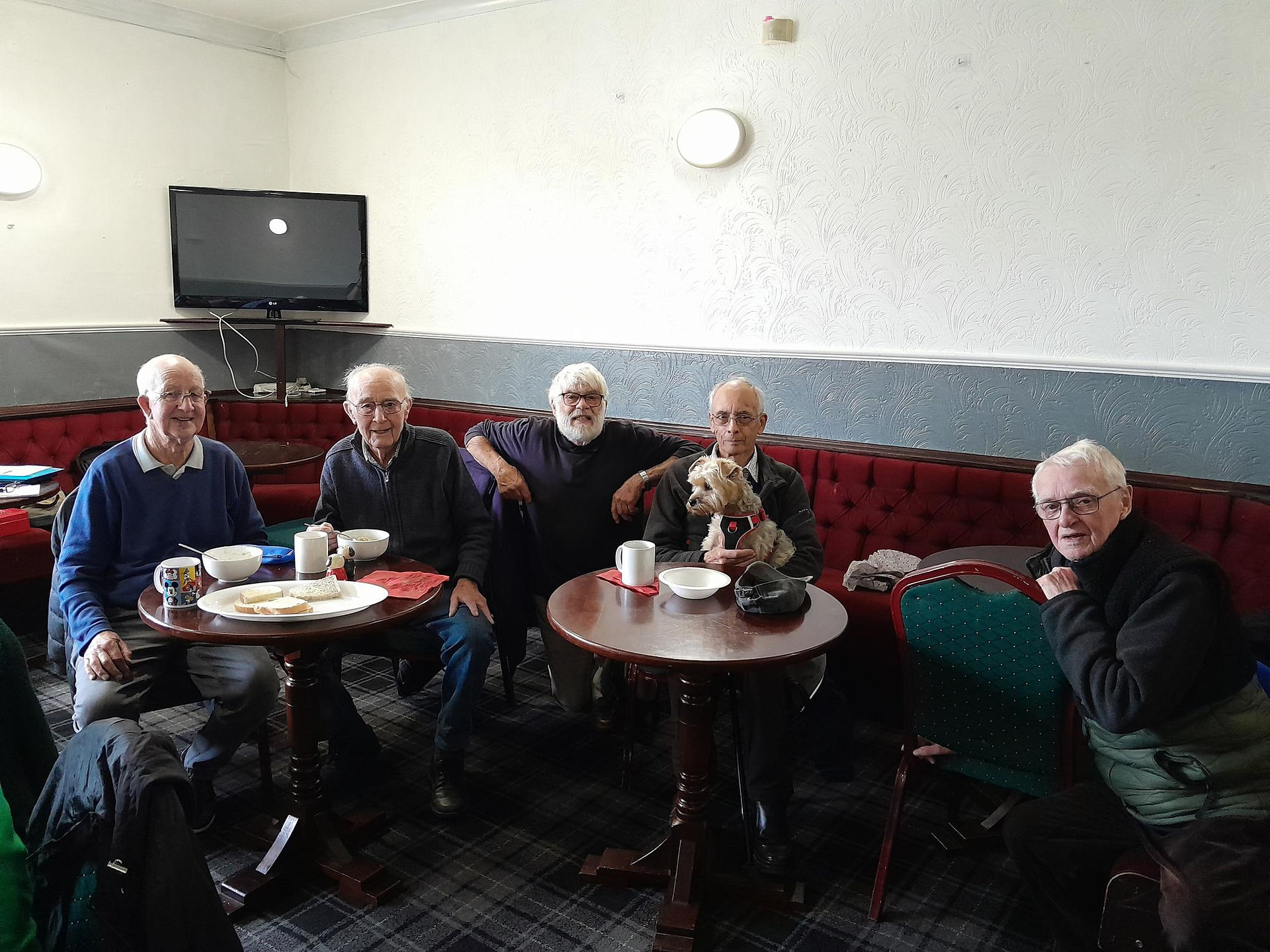 a group of elderly gentlemen smiling around the table chatting