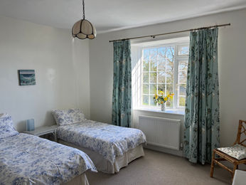 relaxing twin bedroom with fresh cut flowers and views out the window. dressing table and hanging wardrobe space Down House Farm Devon EX6 7SA