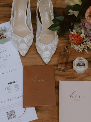 Flat lay of disco wedding details featuring elegant stationery suite, rings, disco balls, wildflower bridal bouquet perfume, and delicate styling elements arranged on a wood backdrop in natural light at the Evergreen Gardens
