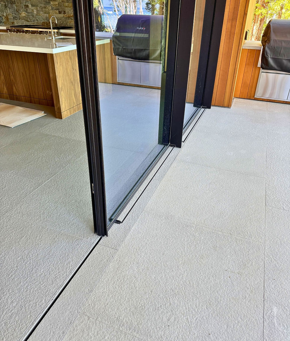 Close up detail of flush threshold sliding door installation showing recessed track at floor level with continuous stone tile surface creating seamless indoor outdoor transition at block frame door opening