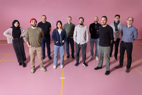 Teamfoto von zwei Frauen und acht Männern die in einer rosaroten Turnhalle in Biel stehen mit Studiolicht.