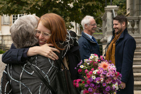 Im Vordergrund die Braut mit einem Blumenstrauss die eine Frau umarmt und im Hintergrund spricht der Bräutigam mit einem Mann vor dem Standesamt in Biel.