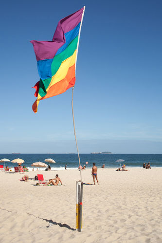 Regenbogenfahne am Strand von Ipanema mit Strandgängern im Hintergrund in Rio de Janeiro, Brasilien.
