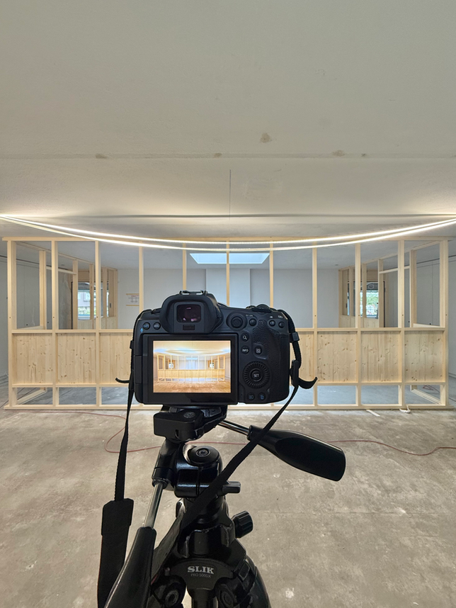 Im Vordergrund sieht man eine Kamera auf einem Stativ. Dahinter sieht man einen Teil einer Baustelle in Biel mit einer Holzkonstruktion.