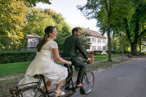 Auf diesem Hochzeitsfoto sieht man ein Brautpaar, welches auf einem alten Tandem Velo die Schüss Promenade in Biel herunterfährt. Vorne auf dem Fahrrad sitzt der Bräutigam und hinten die Braut in ihren schönen Hochzeitskleidern.