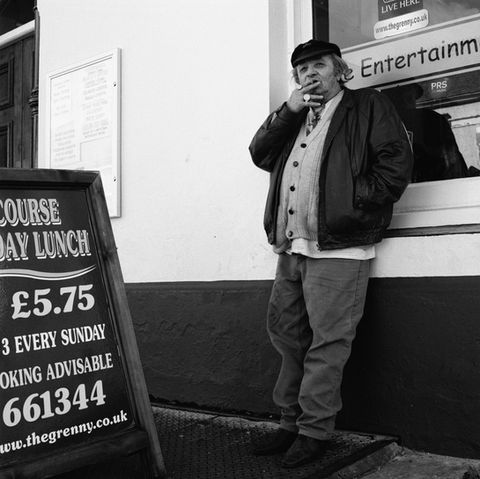 Portrait eines Mannes der am rauchen ist vor einem Pub im St. Judes Quartier, Plymouth, England, schwarz weiss Foto.