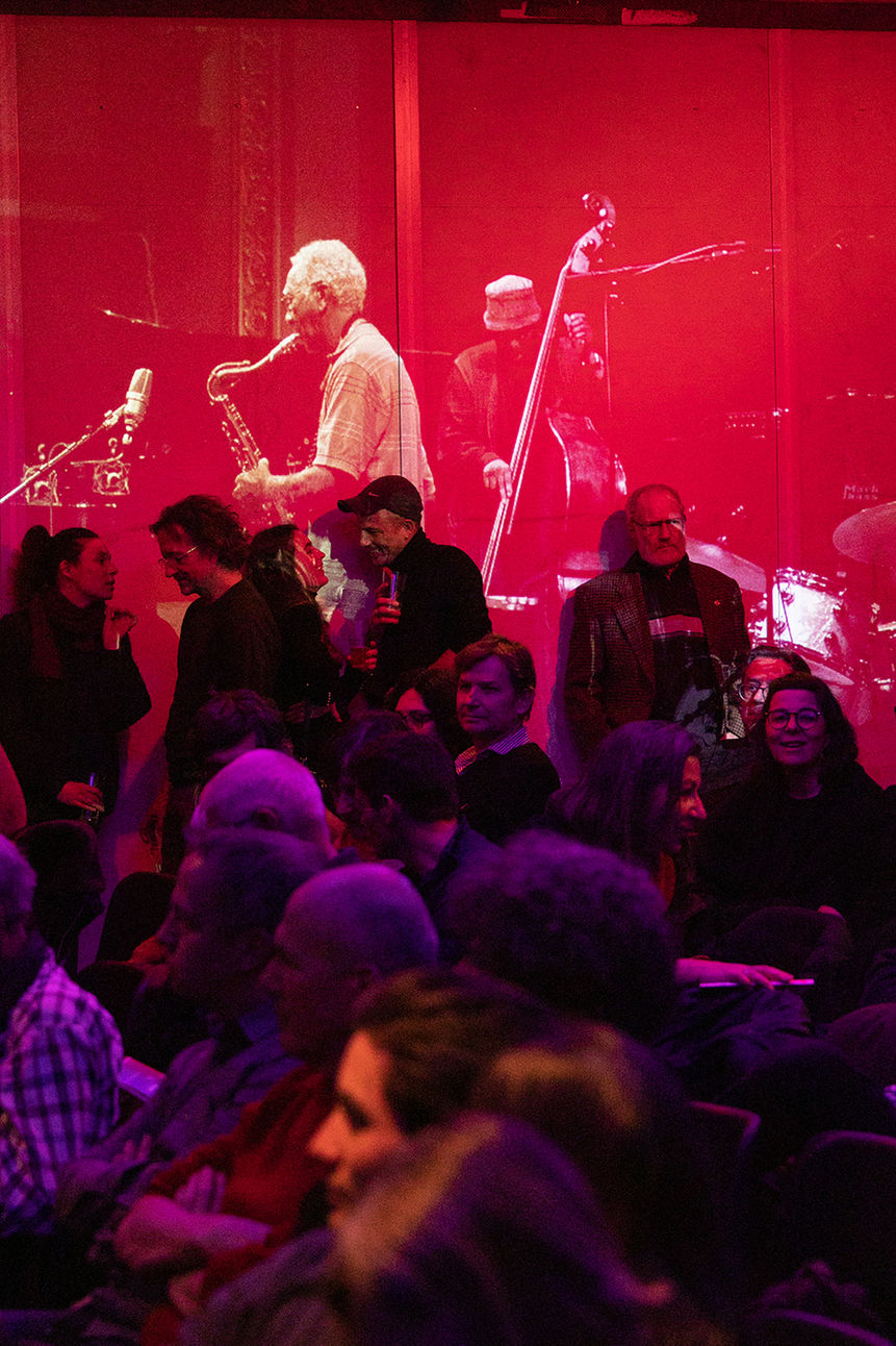Leute aus dem Publikum des Ear We Are Festivals vor einer Wand mit einem in rot Tönen projiziertem Foto einer Band beim musizieren in Biel.