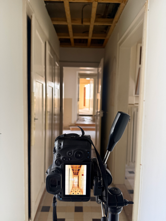 Im Vordergrund sieht man eine Kamera auf einem Stativ. Diese ist auf einen Korridor mit mehreren Türen gerichtet in einem Haus in Biel/Bienne.