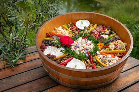 Ein farbiger Antipasti, Käse, Wurst, Tapenaden und Oliven Kübel aus Eichenholz auf einem Holztisch mit Olivenzweigen dekoriert für ein Lebensmittel-Geschäft mit Marktständen fotografiert.