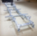 A newly galvanized Land Rover Defender chassis frame placed on a workshop floor, ready for assembly. The silver metallic surface indicates rust-resistant zinc coating, typical in vehicle restorations or rebuilds.