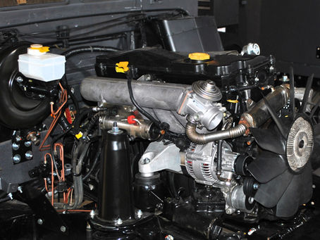 Close-up of a Land Rover TD5 engine installed in a Defender undergoing restoration, showing detailed components including turbo, fan, and fuel system during rebuild process
