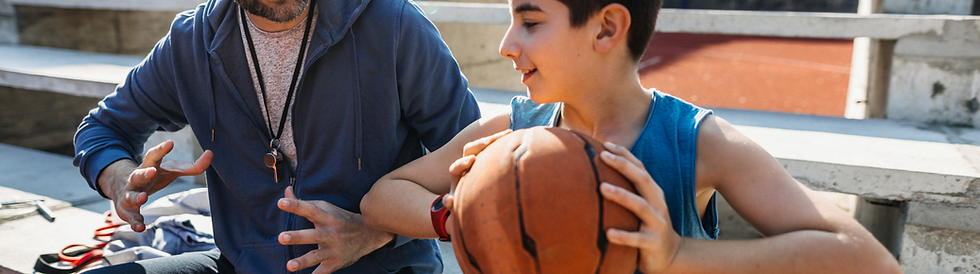 a teenaged boy being shown how to properly hold a basketball by his coach