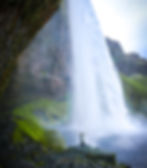 Seljalandsfoss waterfall in Iceland during the midnight sun with a girl standing underneath the powerful waterfall.