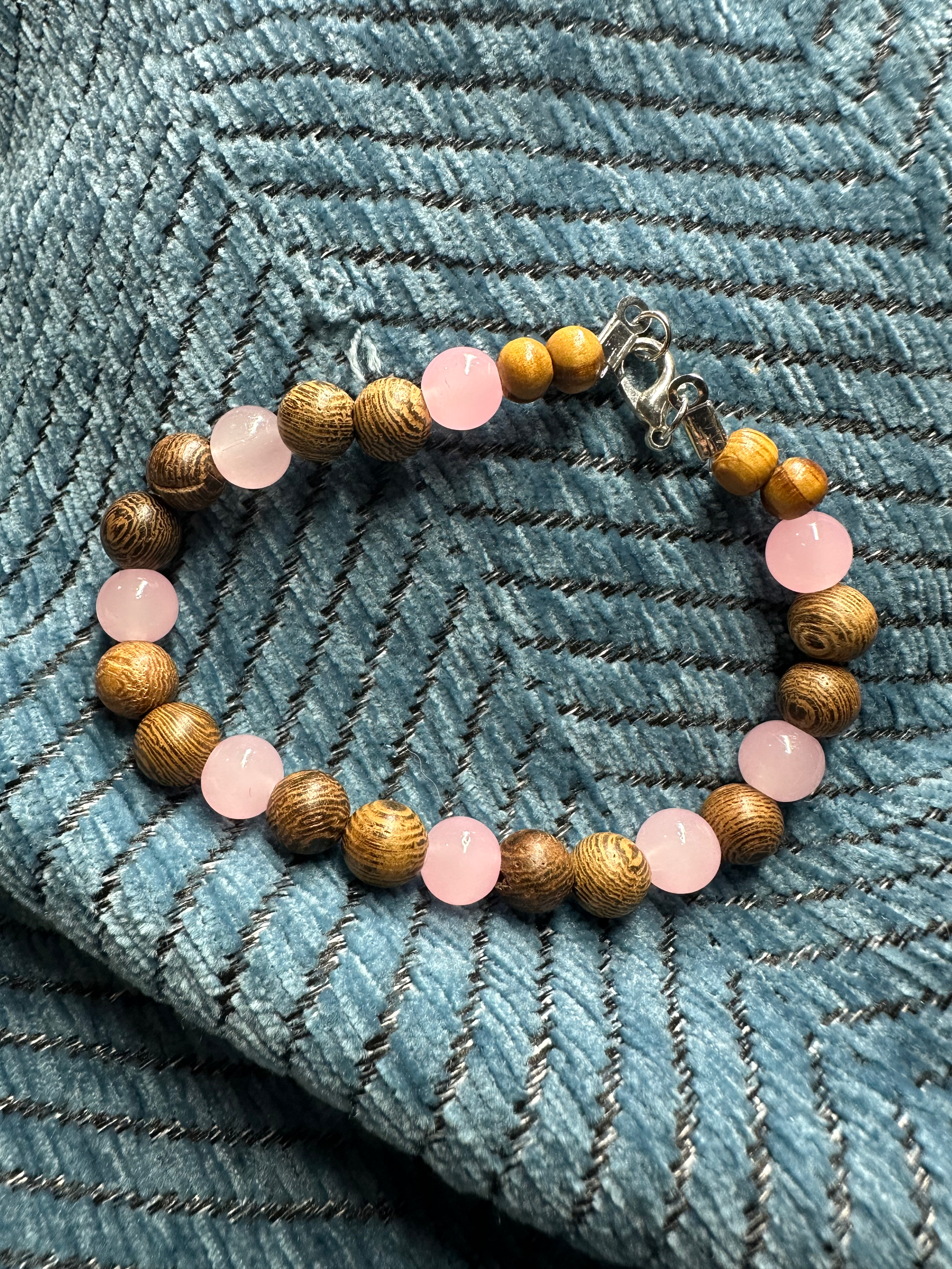 beaded bracelet featuring alternating wooden and translucent pale pink beads. finished with a silver lobster claw clasp
