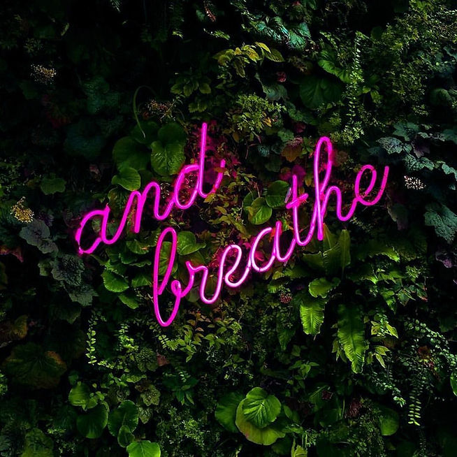 foliage wall with pink lettering on top which reads "and breathe"