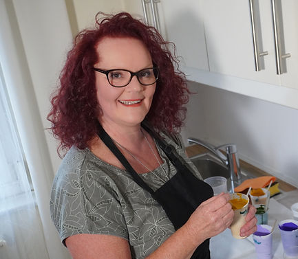 Michaela Berger mischt die Acrylfarben Gelb, Gold, Lila und Dunkelblau in einem Becher mit einem Pouringmedium.