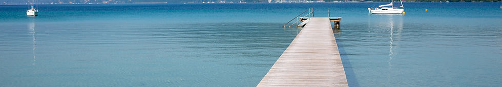 Blick über den blauen Attersee mit einem Steg und Booten im Vordergrund