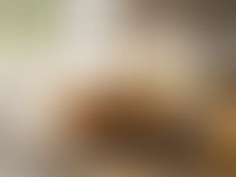 A sliced frosted layer cake on a plate, surrounded by a whisk, a spatula, eggs, a can of Sweet Cow creamer, and baking items on a wooden table.