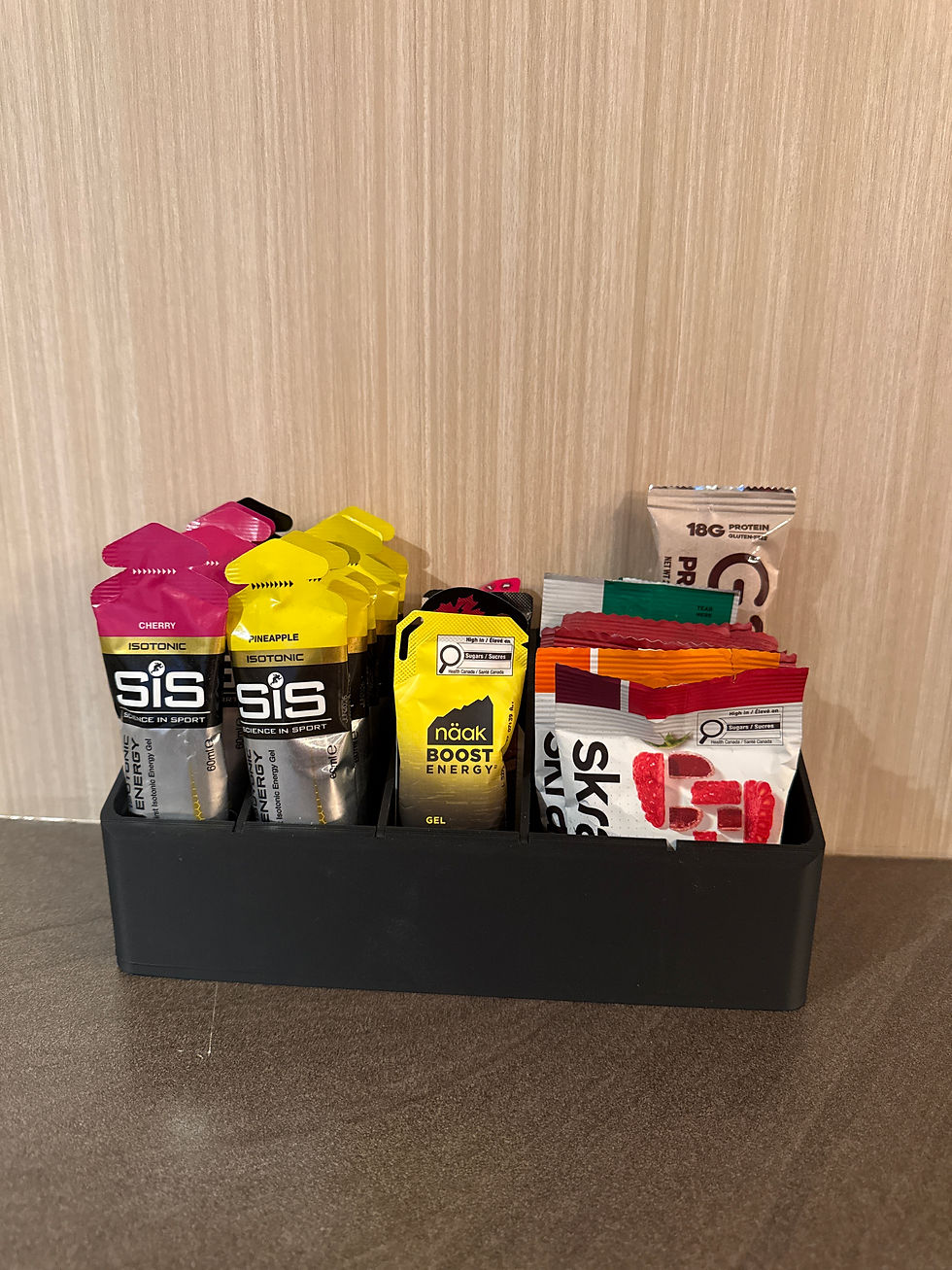 Organisateur noir mat pour gels énergétiques, électrolytes, jujubes et barres de nutrition sportive posé sur un comptoir.