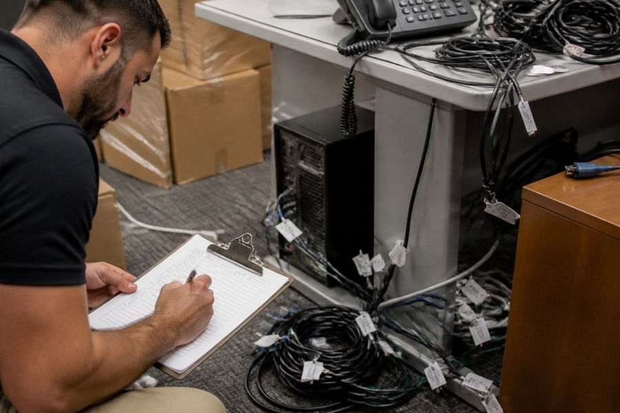 Employee organizing and labeling cables while moving office equipment in a workspace