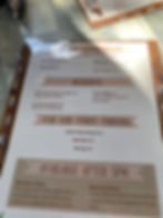 Menu on a table with items for kids, desserts, pet meals, and evening specials. Includes BBQ chicken and salmon. Sunglasses nearby.