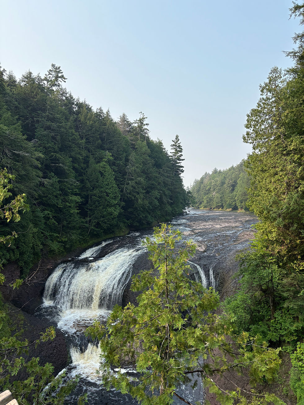 Waterfall cascades over rocks surrounded by lush green forest under a clear blue sky, creating a serene and peaceful atmosphere.